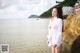 A woman in a white shirt standing on a rock by the water.