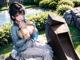 A woman sitting on a bench next to a trash can.