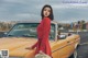 A woman in a red dress standing next to a yellow car.