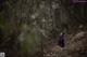 A woman in a black dress walking through a forest.