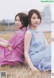 A couple of women sitting on top of a grass covered field.