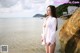 A woman in a white shirt standing on a rock by the water.