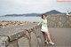 A woman leaning against a stone wall by the water.