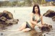 A woman in a bikini sitting on a rock in the water.